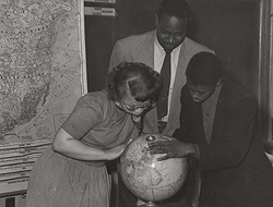 Andrew Foster standing over two students peering over a globe.