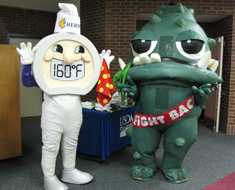 Image: Oversized cartoon-style characters—good guy Thermy (giant thermometer prompting cooking to safe meat temperatures) and bad guy Bac (short for bacteria)—mingled with the children.

