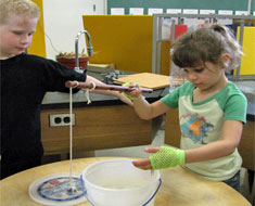 Image: KDES student Freddy Scott watches while Aliza Castro-Selzer tries out his “Funny Fish” paper clip and magnet experiment. 