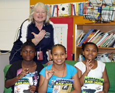 Image: KDES librarian Cynthia Sadoski signs THANKS while KDES students fingerspell R-I-F, expressing their appreciation to Reading Is Fundamental. (Photo: Susan Flanigan)