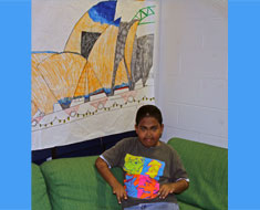 Image: Fourth grader Christian Leggett makes the sign for "Australia" in front of his drawing of the Sydney Opera House. Leggett researched Australia for his ESY country project. His teacher Heidi Burns complimented the drawing, saying, "Christian thinks and draws like an engineer." (Photo: Susan Flanigan)