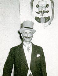 David Peikoff wearing a tux with a tie and vest, with a hankerchief in the left chest pocket. He has a top hat and a large mustache, which appears to be fake.