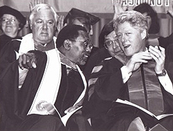 Glenn Anderson and President Bill Clinton in graduation robes, chatting. Anderon is pointing outward, toward the students