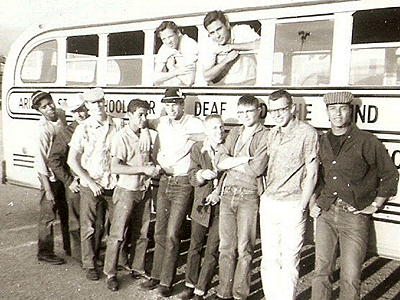 Arizona School for the Deaf and Blind. Two boys leaning out of bus windows, while seven boys lean against the bus.