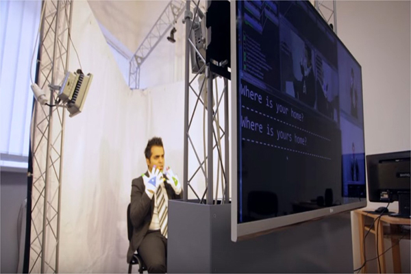 man sitting behind a large monitor signing with special gloves