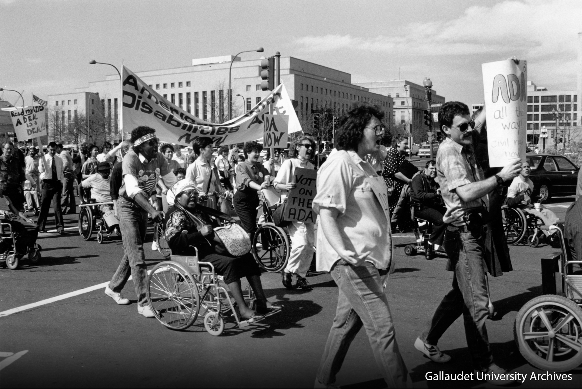 Many diverse protesters of disabilities marching on the streets holding signs.