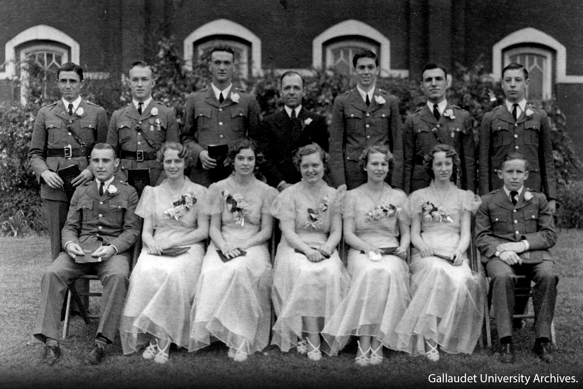 Group photo of male soldiers standing while five women sit.