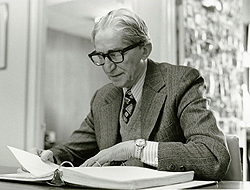 David Peikoff, sitting at a desk reading through a binder. He's got a suit with a sweater and tie. He's older now, has black glasses.