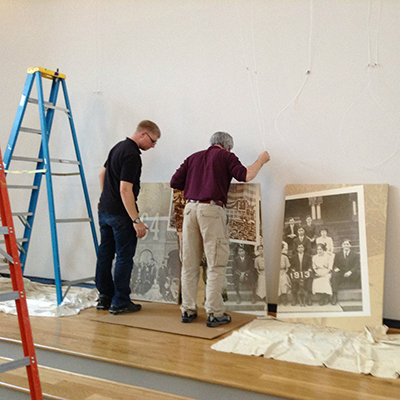 Two men, surrounded by a ladder and some panels in preparations of building a banner for the exhibit.