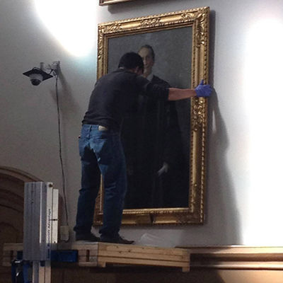 Professional archivist removes a portrait from the wall, carefully.