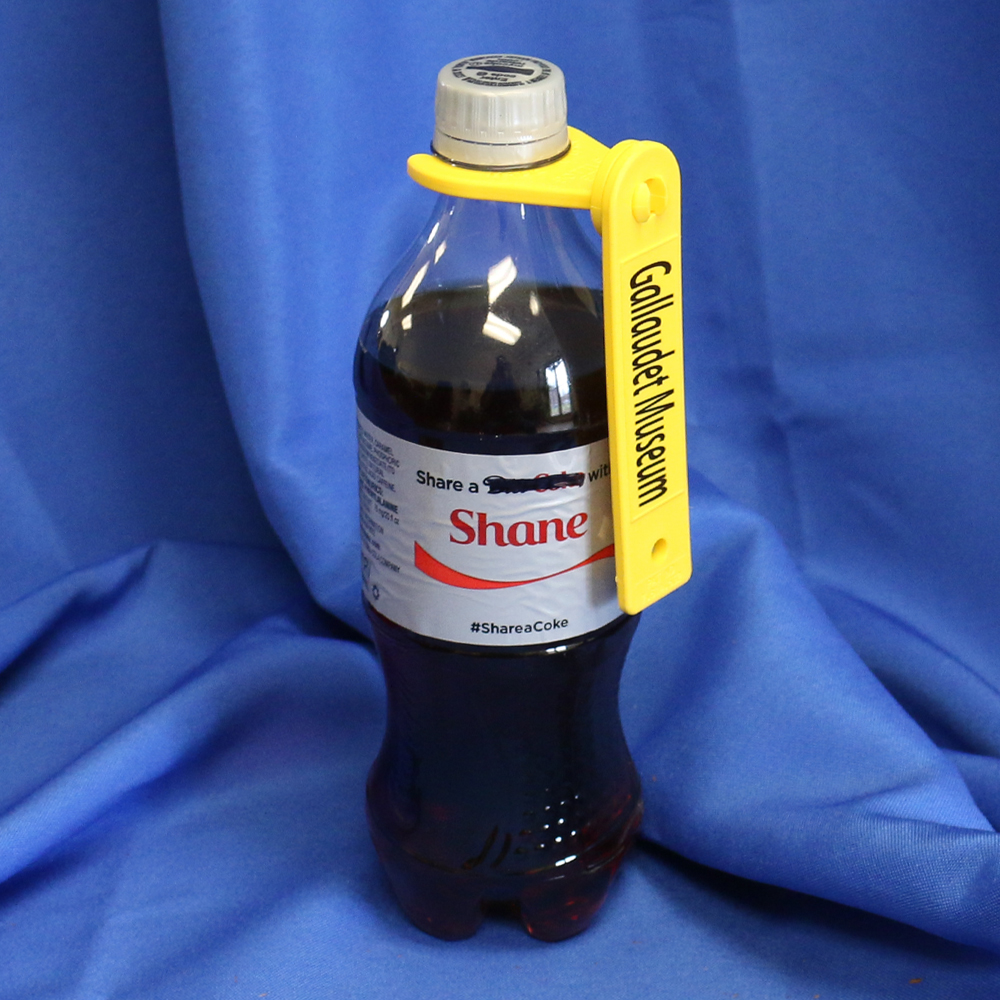 Yellow bottle holder attached to a Coke bottle - it says "Gallaudet Museum" on it.